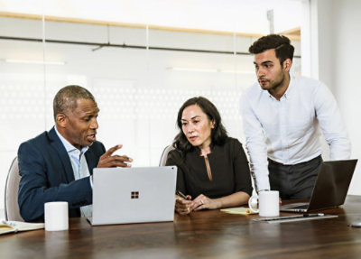 Three people sitting in an office looking at a laptop.